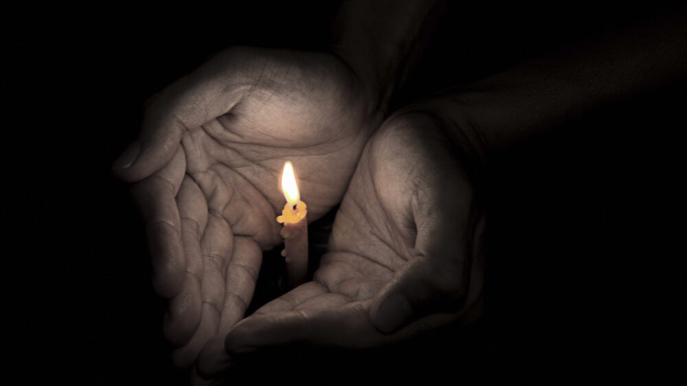 Huumeisiin kuolleiden muistopäivä (kuva käsistä, jotka suojaavat kynttilää tuulelta)